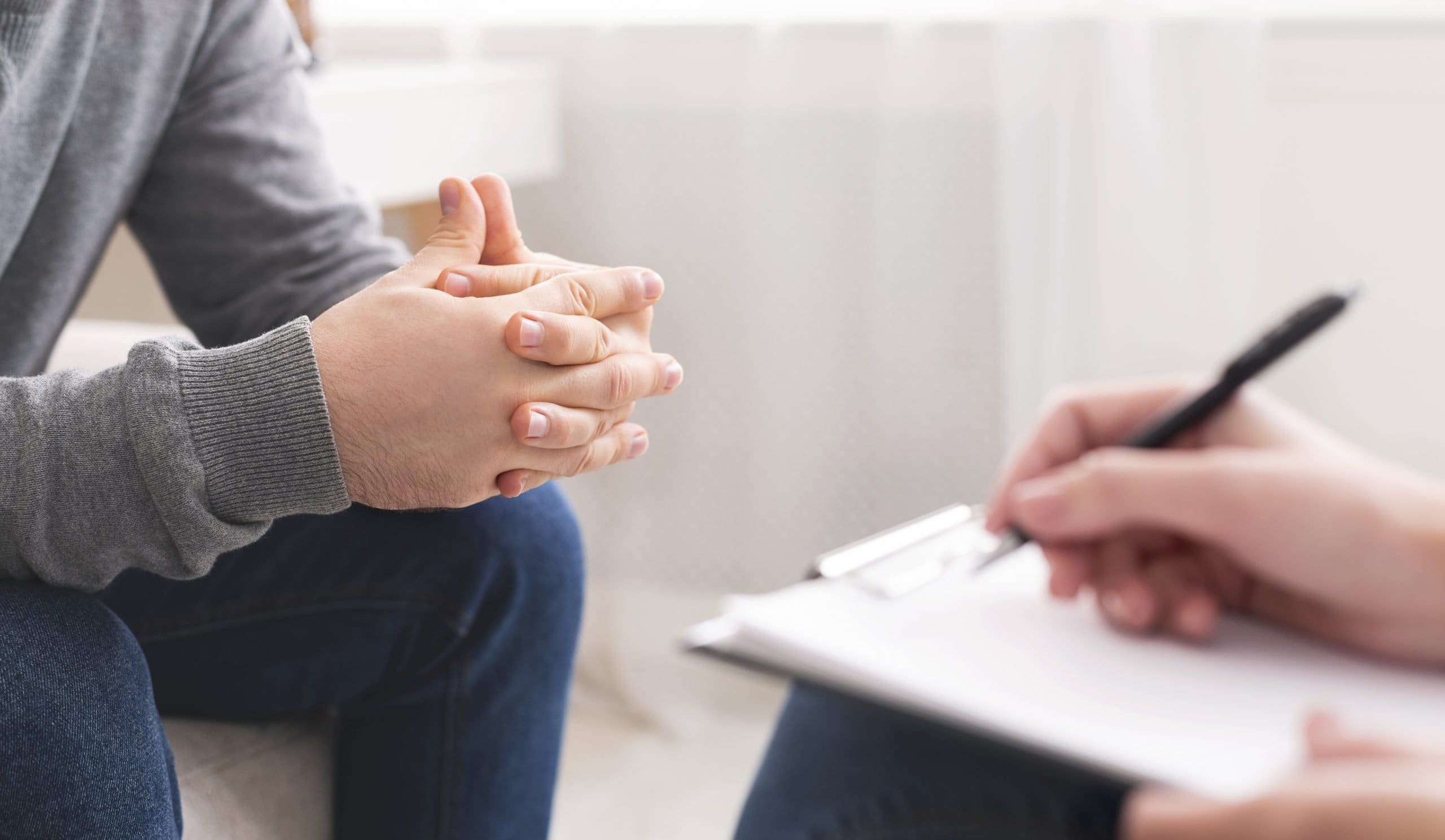 Therapist writing notes during counseling session with single man REACH Individual Counseling